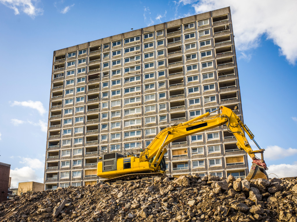 An excavator breaking ground in front of a tall building under construction
